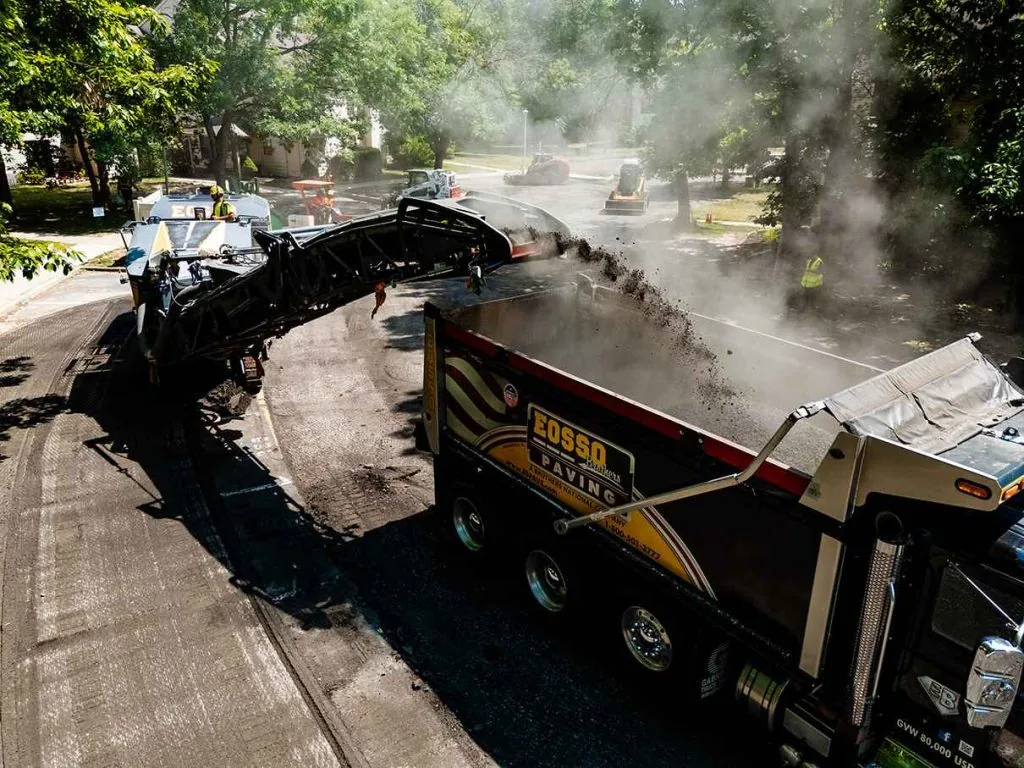 asphalt paving project, two trucks with a machine putting asphalt millings into back of the other truck