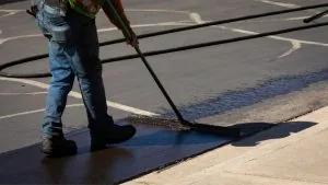 worker brushing asphalt sealcoat on to pavement