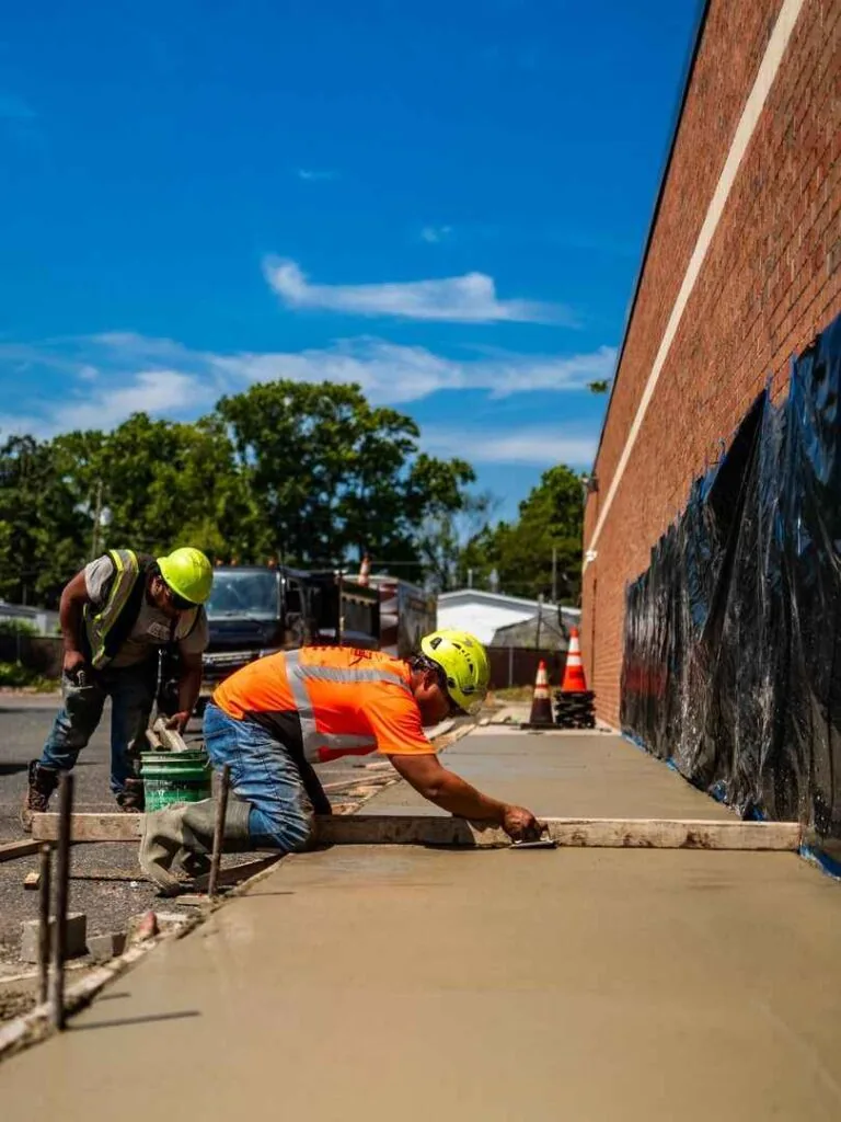 concrete paving contractor working on a new sidewalk with a level to make sure sidewalk is straight