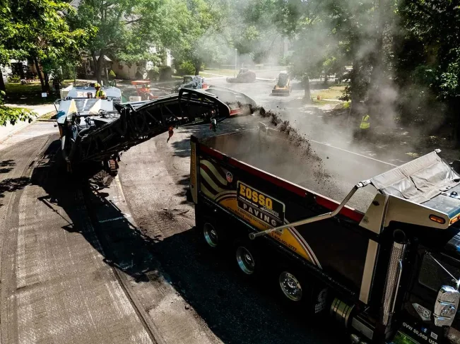 asphalt paving project, two trucks with a machine putting asphalt millings into back of the other truck