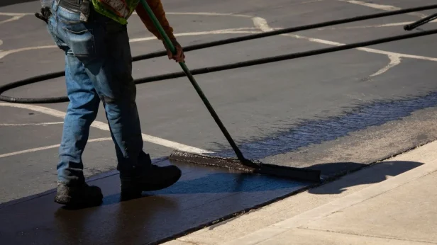 worker brushing asphalt sealcoat on to pavement